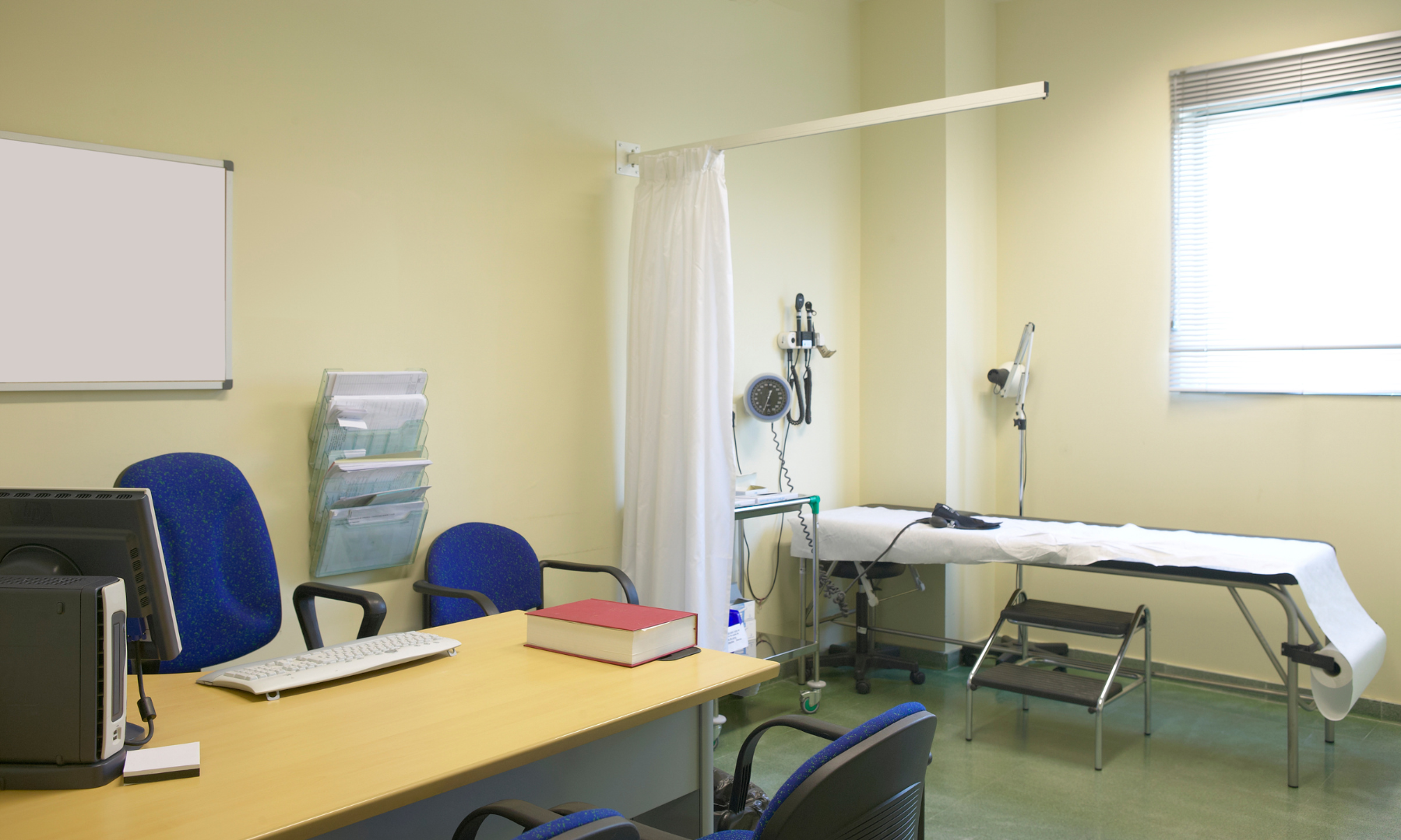 A consultation room fitted out with desk, examination couch and privacy screen