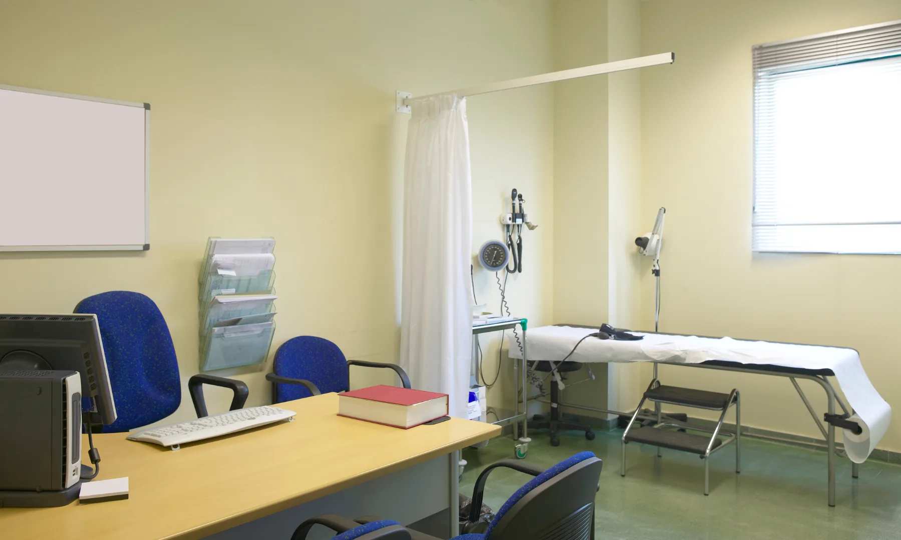 A consultation room fitted out with desk, examination couch and privacy screen
