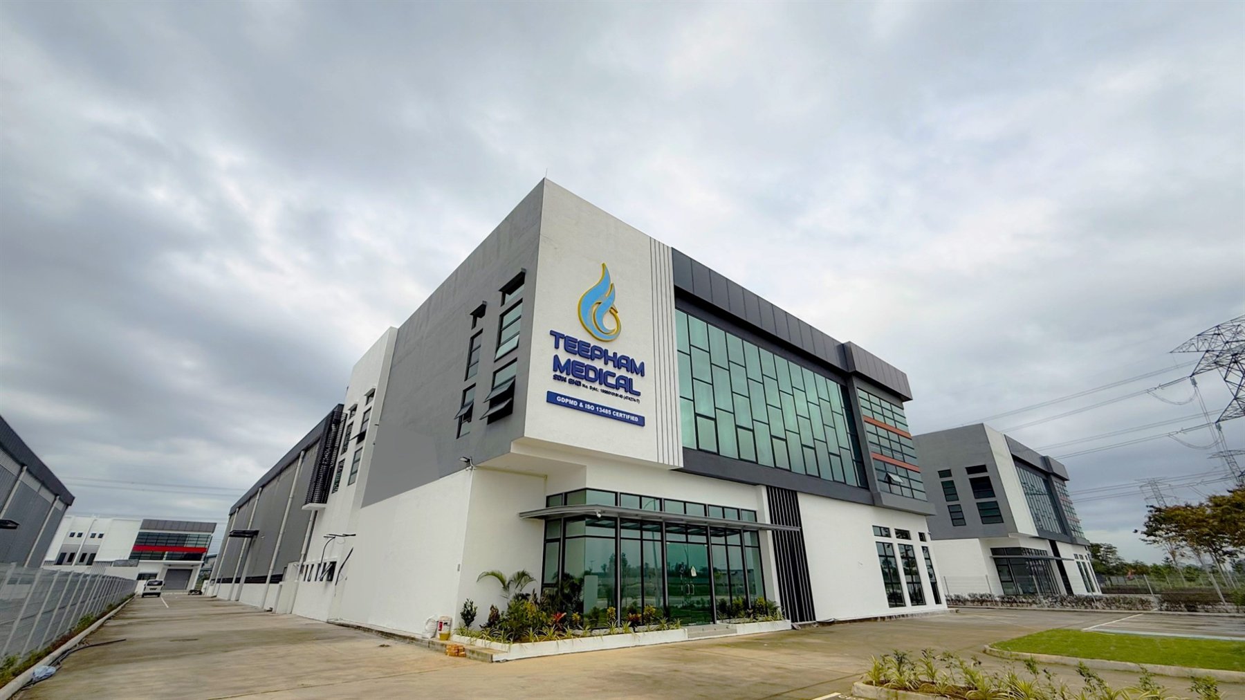 Side view of the Teepham Medical head office in Kota Seri Langat, Selangor, showing the signed corner tower, glass frontage and the warehouse behind